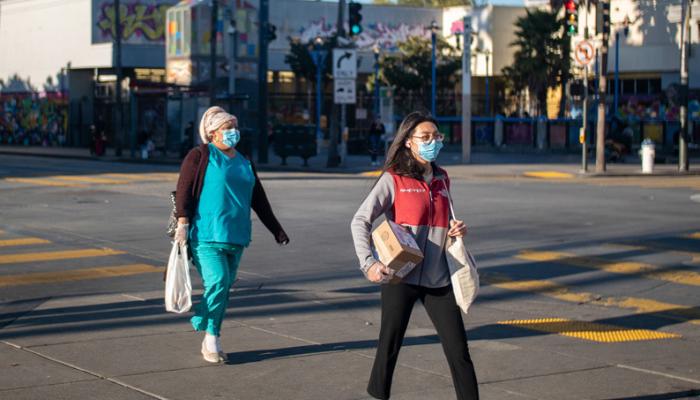 Two women wearing protective masks walking at crosswalk on 16th Street in the Mission District