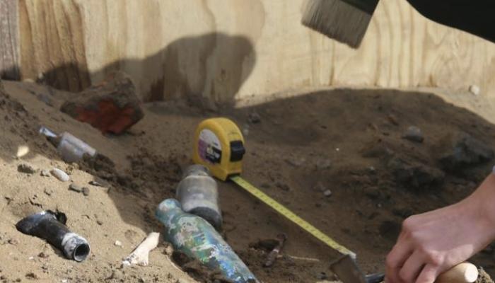 Broken bits of old bottles being excavated from dirt by archaeologist.