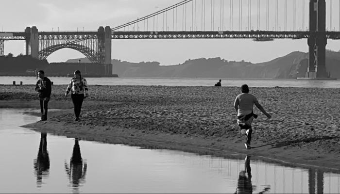 Black and white photo of people walking along the beach at Marina Green