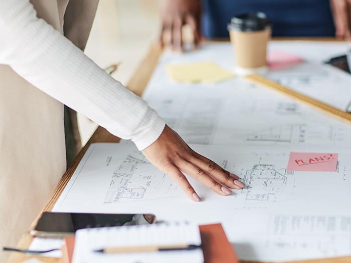 woman's hand runs over architectural plans laying on a desk