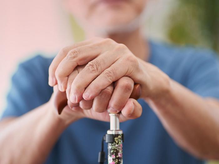 An older person's hands resting on a colorful cane handle.